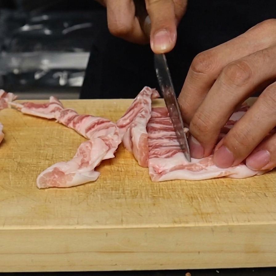 生の豚バラ肉をまな板の上で1cm幅に切り揃える様子。