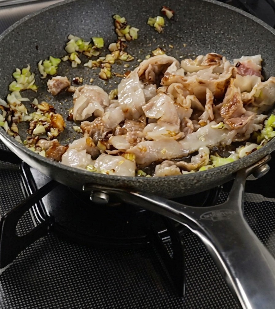 豚バラ肉と野菜を箸で混ぜながら、肉に焼き色がつくまで炒める様子。