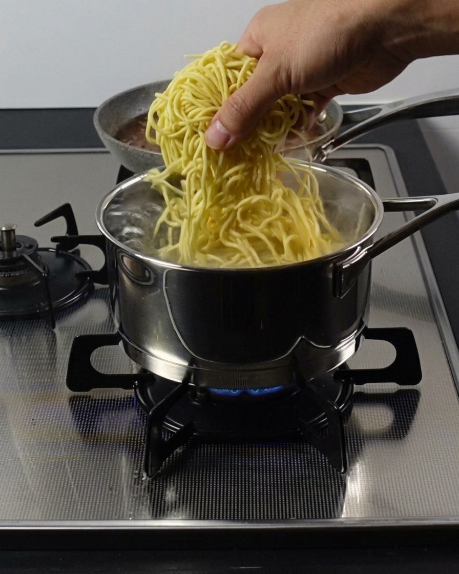 沸騰した鍋に、黄色い太めの中華麺を入れる様子。