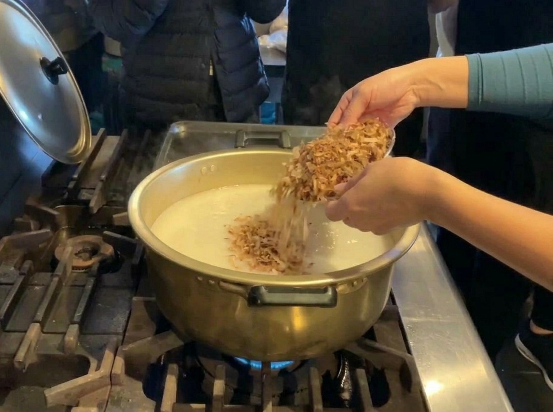 白いスープが入った大きな鍋に、ボウルから大量のかつお節を投入している様子。