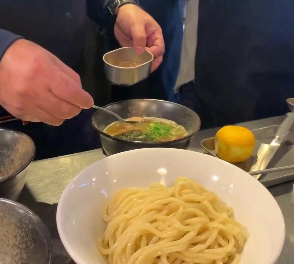 スープの中央にスプーンで魚粉を盛り付け、ネギを添えて仕上げる様子。