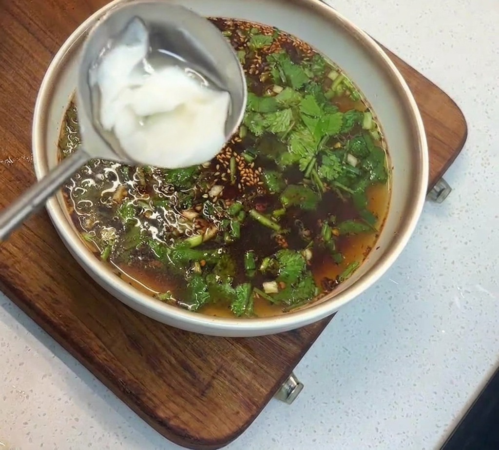 ハーブが浮かぶスープの中に、お玉に入った白い固形のラードを沈めようとしている様子。