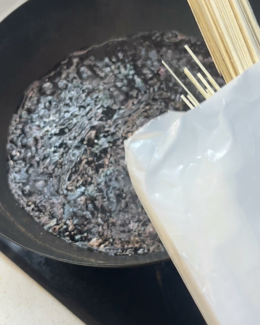 沸騰した黒い中華鍋に、真っ直ぐな白い乾麺の束を入れている様子。