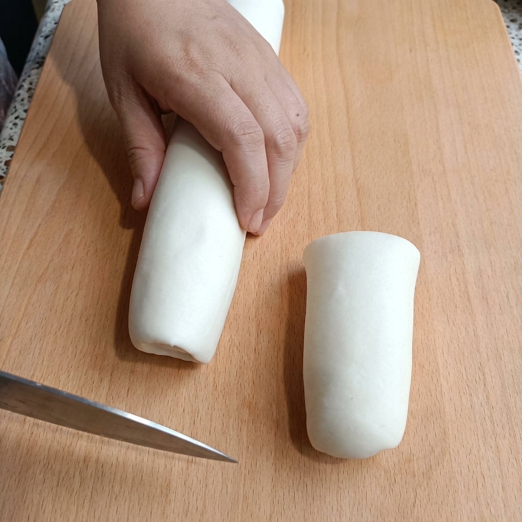 まな板の上で棒状に伸ばした生地を包丁で切る様子