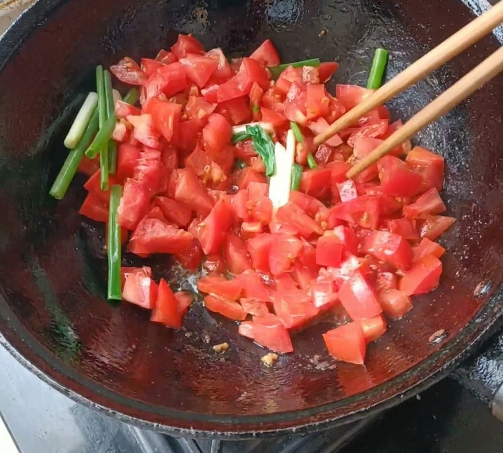 中華鍋でトマトとねぎを箸を使って炒める様子