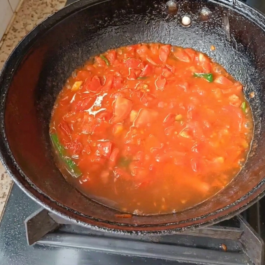 中華鍋の中でトマトとねぎが煮込まれている様子