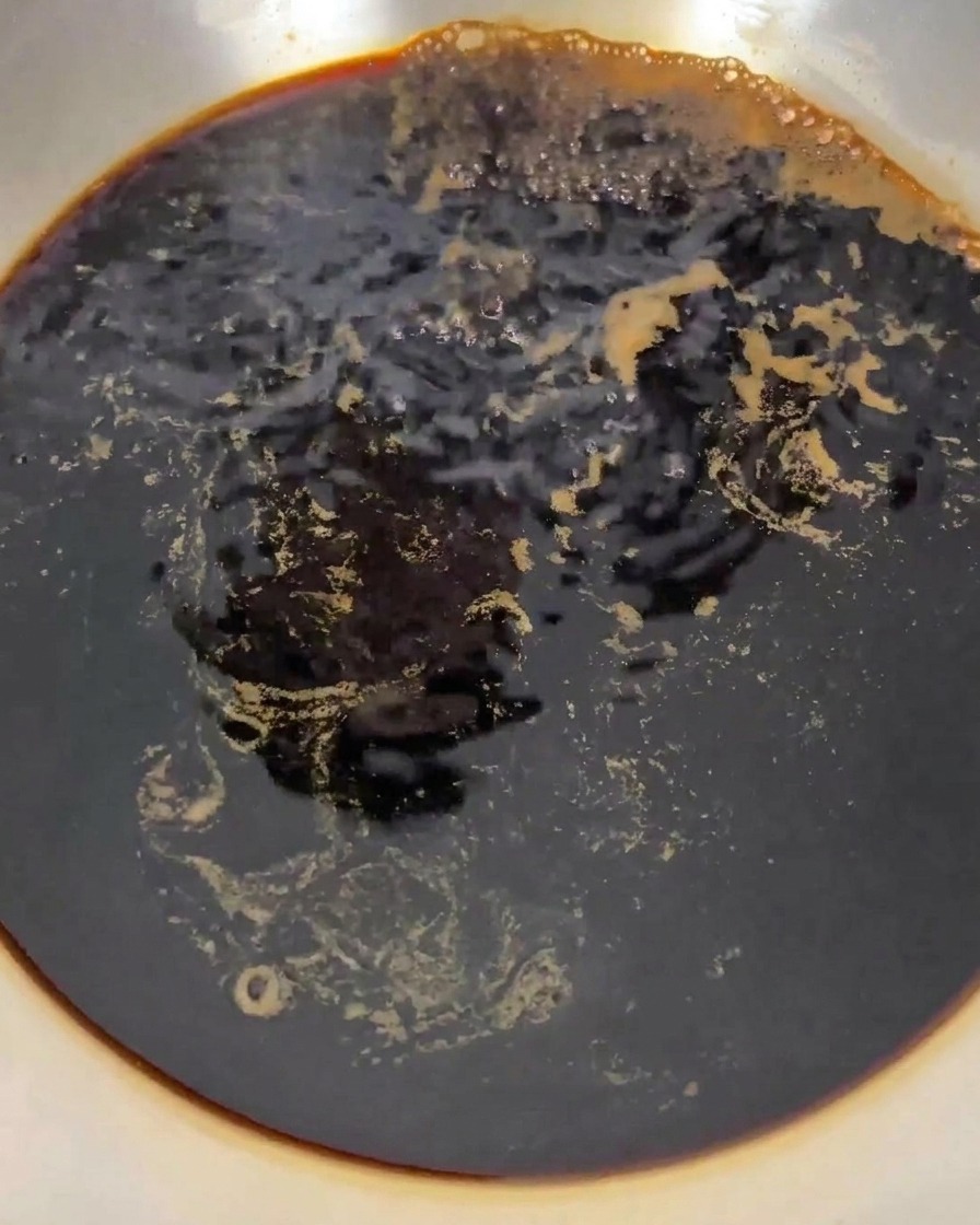 コンロの上で、鍋の中の濃い色の液体が激しく沸騰している様子。