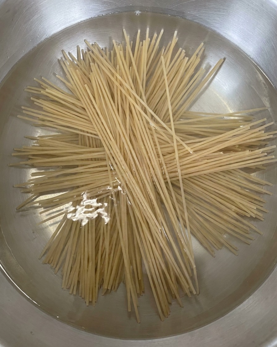 沸騰した鍋に、乾麺のそばを放射状に広げて入れている様子。