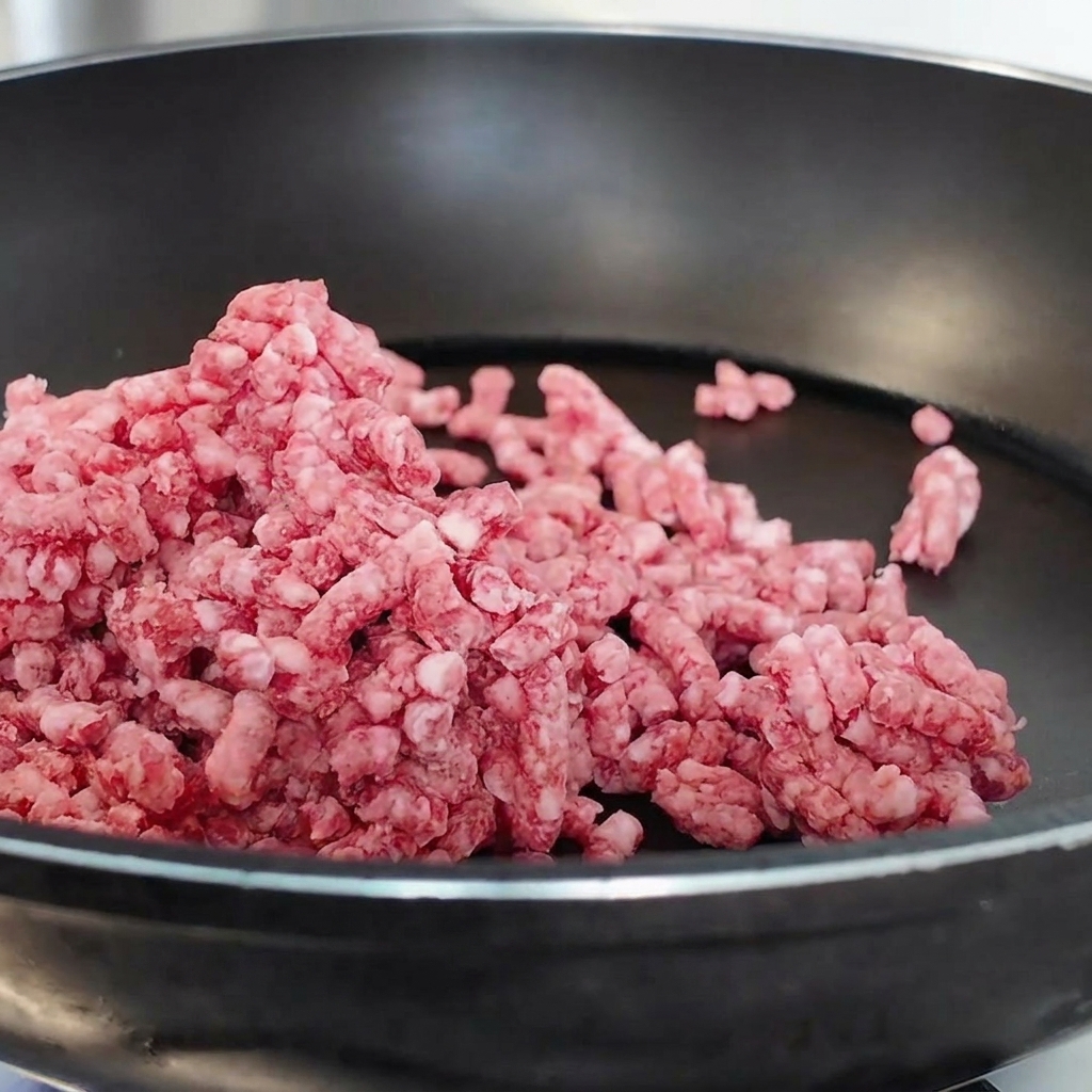 黒いノンスティック加工のフライパンで、生の牛ひき肉をほぐしながら炒めている様子