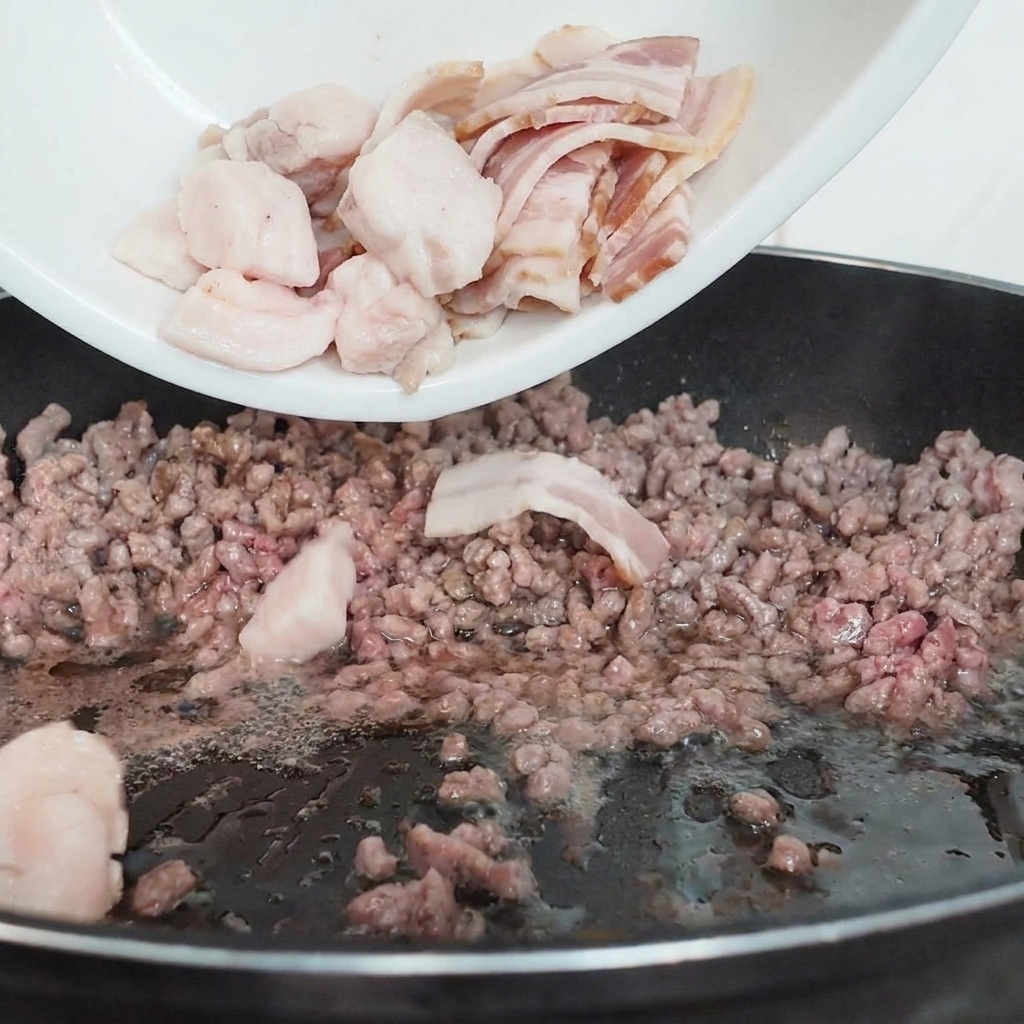 牛ひき肉が入ったフライパンに、スライスしたマッシュルームを加えている様子