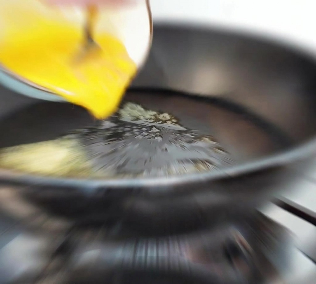 バターが溶けた熱いフライパンに、卵液を注いでいる様子