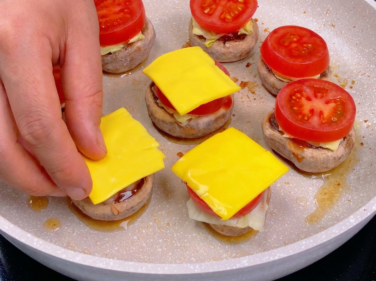 重ねられたミニバーガーのトマトの上に、四角いスライスチーズを手で丁寧にのせている様子。