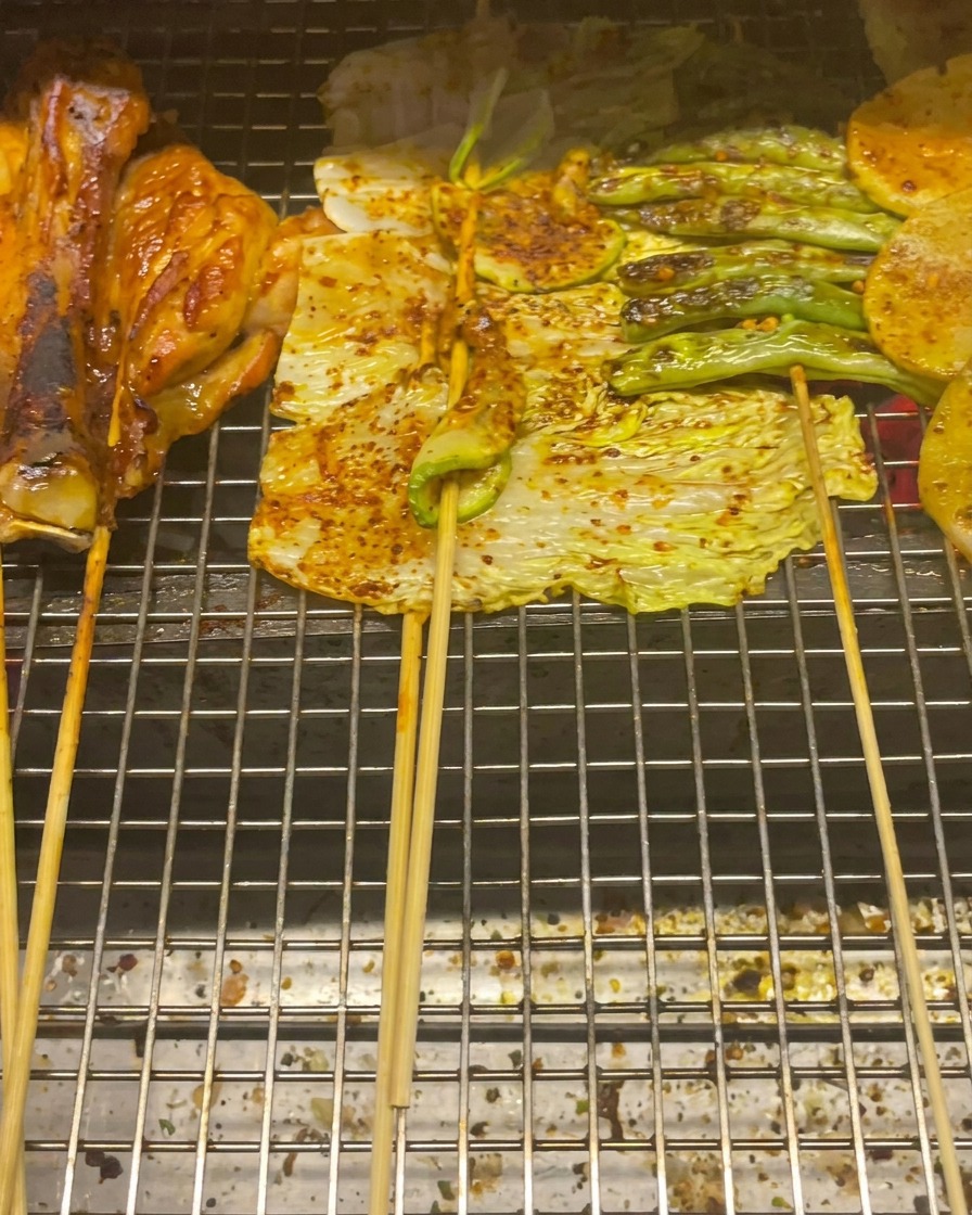 鶏もも肉、キャベツ、ズッキーニ、いんげん、じゃがいもを網で焼いている様子