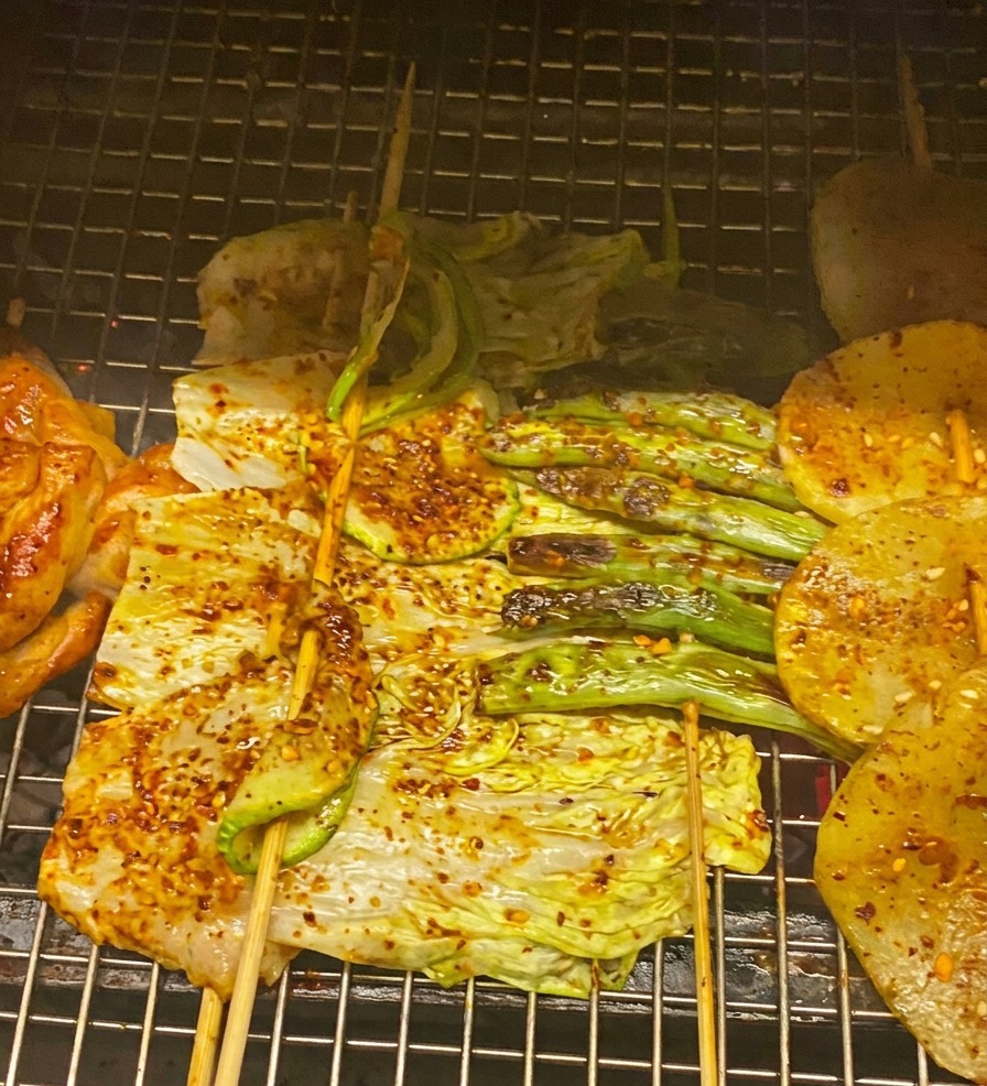 グリルした肉や野菜に赤いBBQソースを塗り、ねぎを散らしているアップ写真