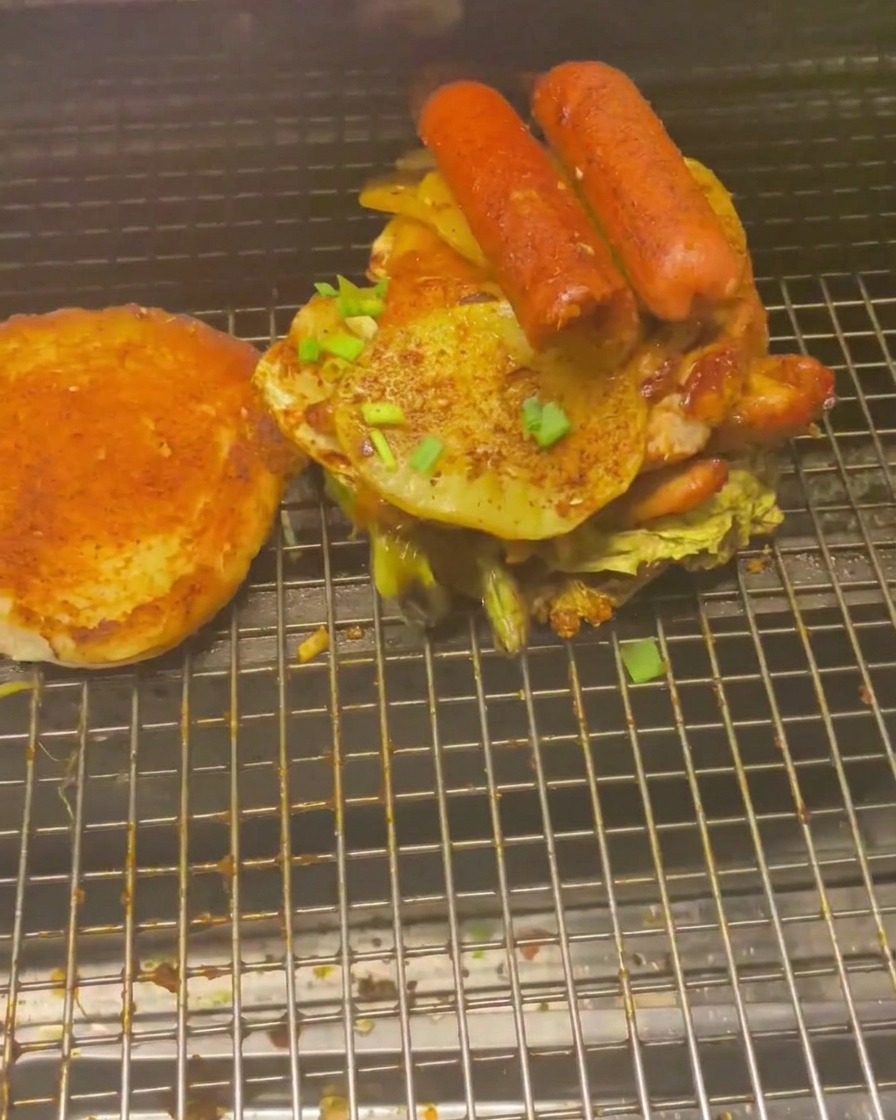 ソーセージやじゃがいもを高く積み上げたバーガーの制作過程