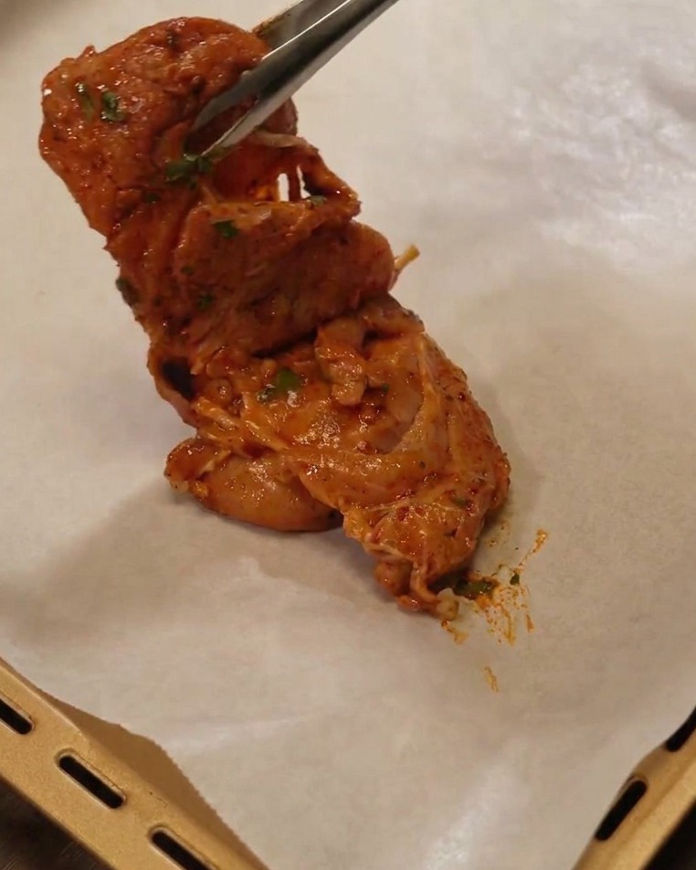 クッキングシートを敷いた天板に、トングでマリネした鶏肉を並べている様子