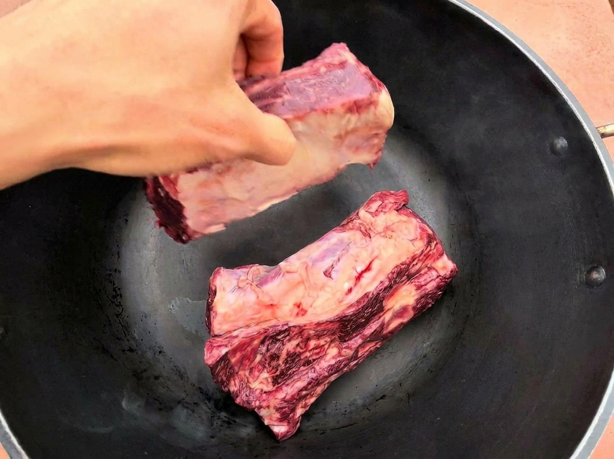 熱したフライパンに大きな牛リブを2枚並べて焼いている様子