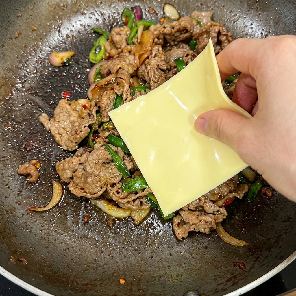 炒めた牛肉の上にスライスチーズを乗せる様子