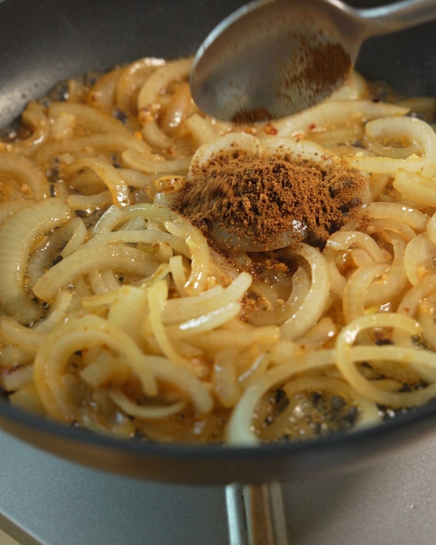 スライスした玉ねぎを炒めながら、ブラウンシュガーや調味料を加えてじっくりと煮詰めている様子。