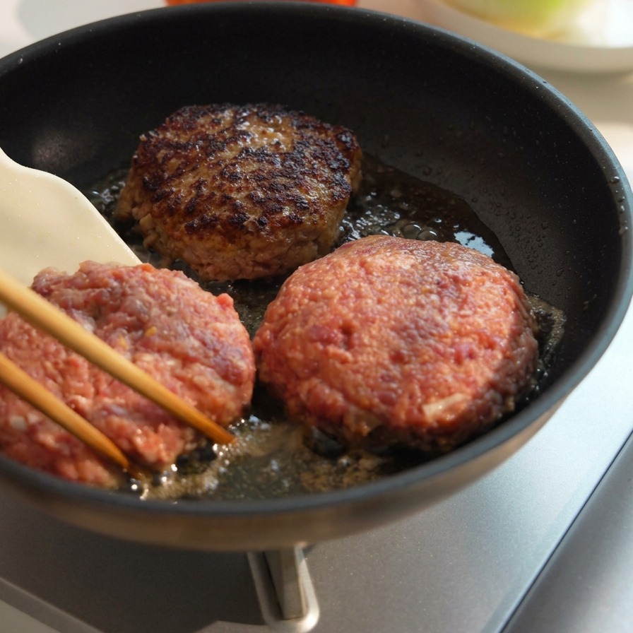 3枚の厚いパティを焼き、片面が香ばしく焼き色がついた状態で裏返している様子。