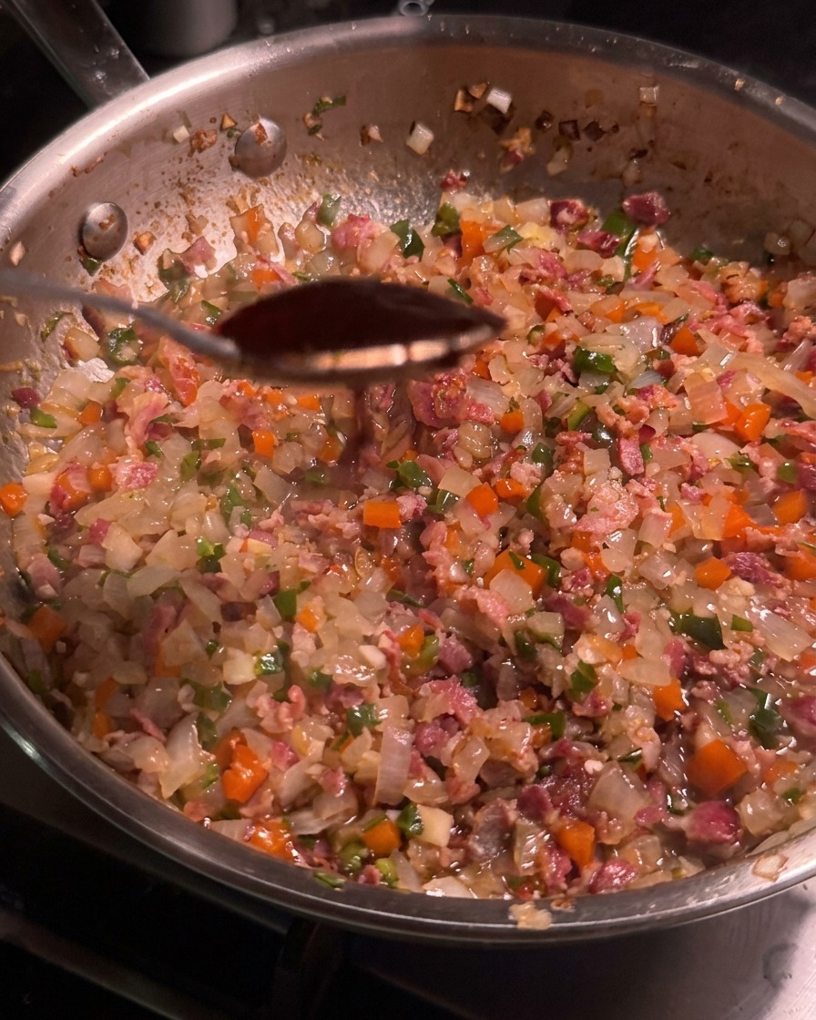 ベーコンや野菜が詰まったフライパンの上で、濃い色のチポトレペッパーソースをすくい上げたスプーンの様子。