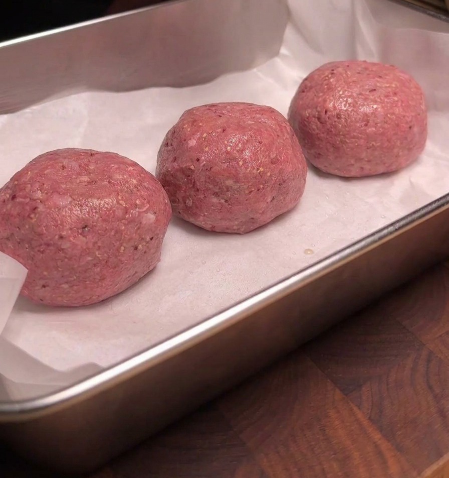 白いクッキングシートに並んだ3つの肉団子の表面に、液体スモークが均一に吹き付けられて艶やかに光っている様子。
