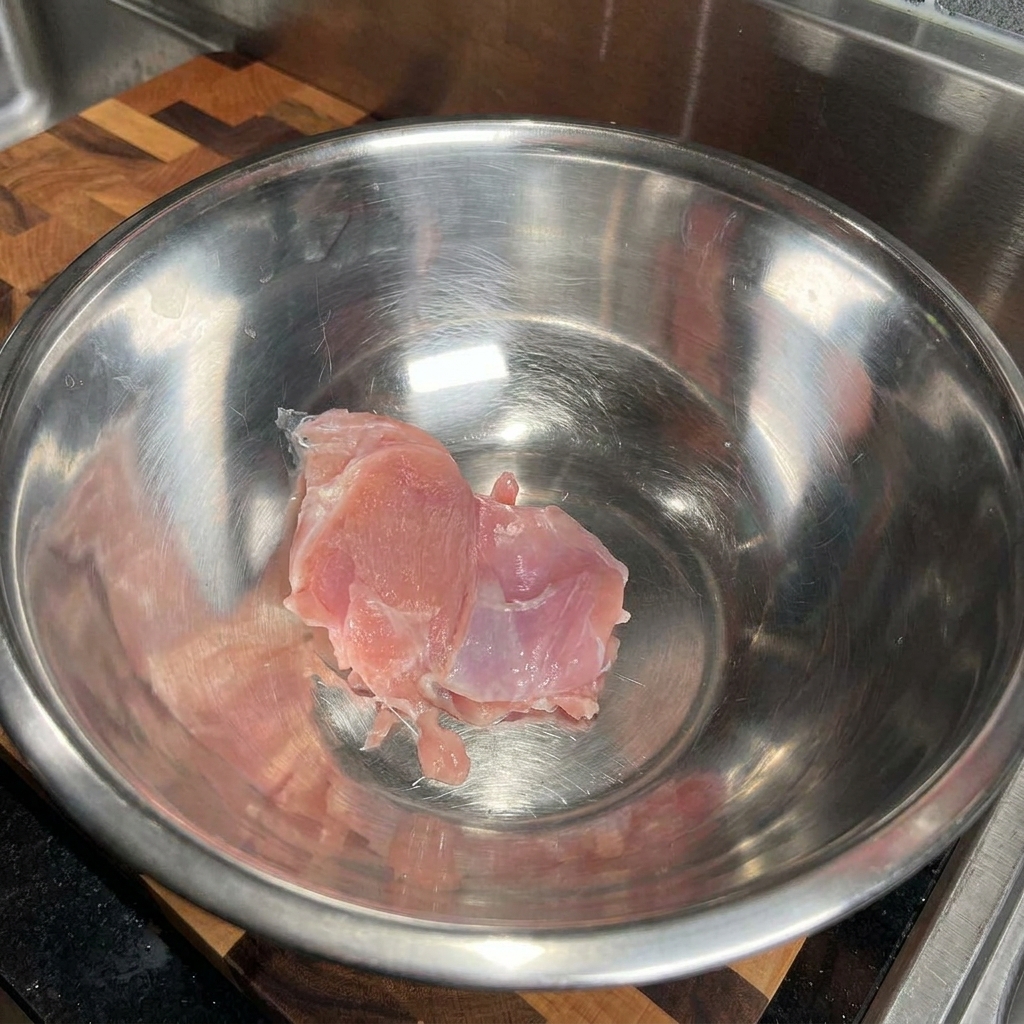 ステンレス製の大きなボウルに生の鶏もも肉を入れている様子。