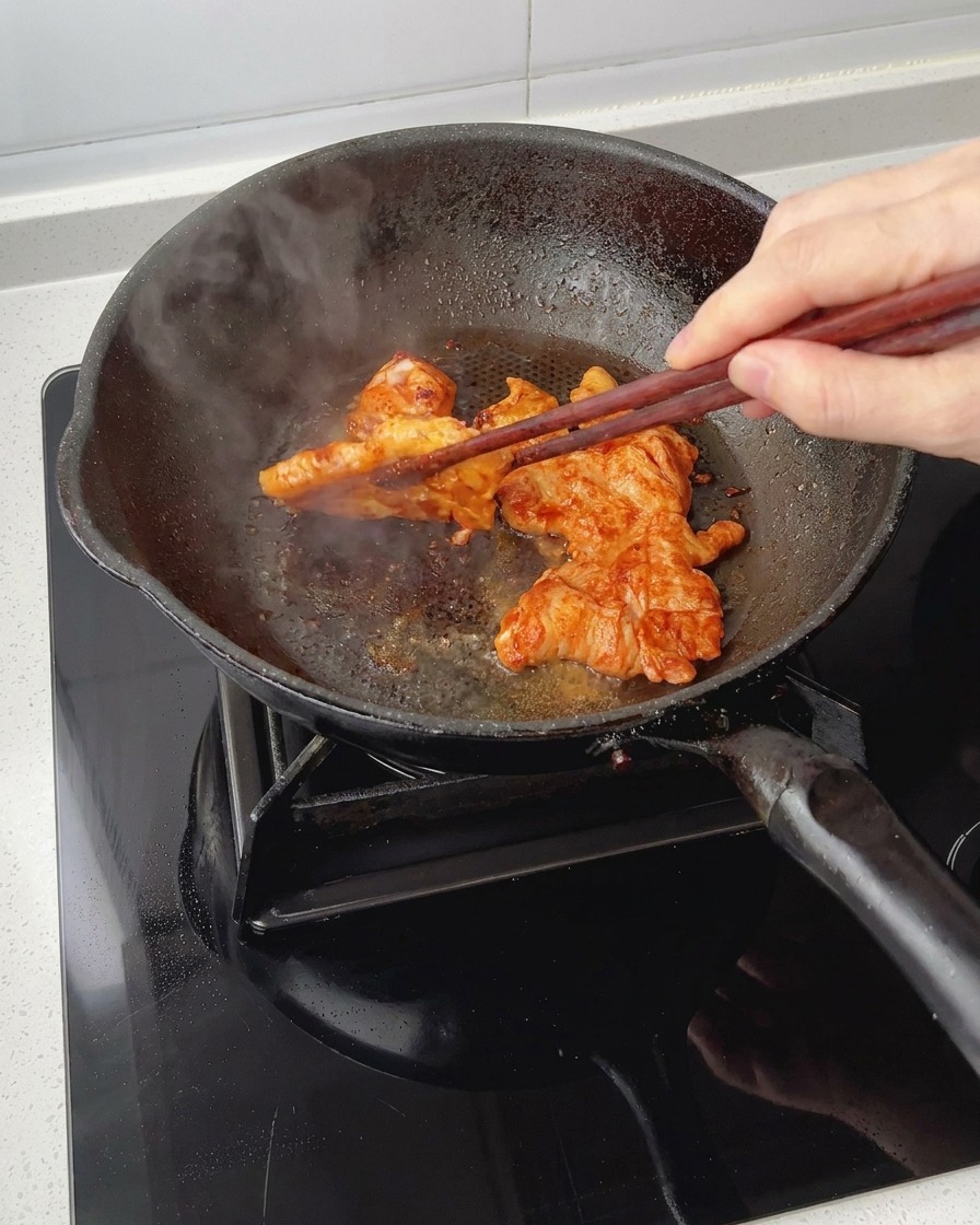 フライパンの中でチキンを箸でひっくり返しながら、表面にツヤのある美味しそうな焦げ目を付けている様子。