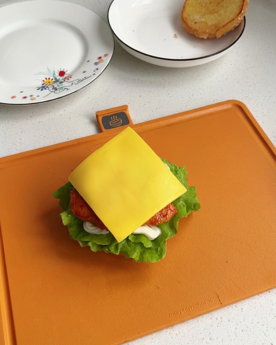 組み立て途中のバーガーの中で、焼き立てのチキンの真上にきれいに乗せられた四角い黄色いスライスチーズ。
