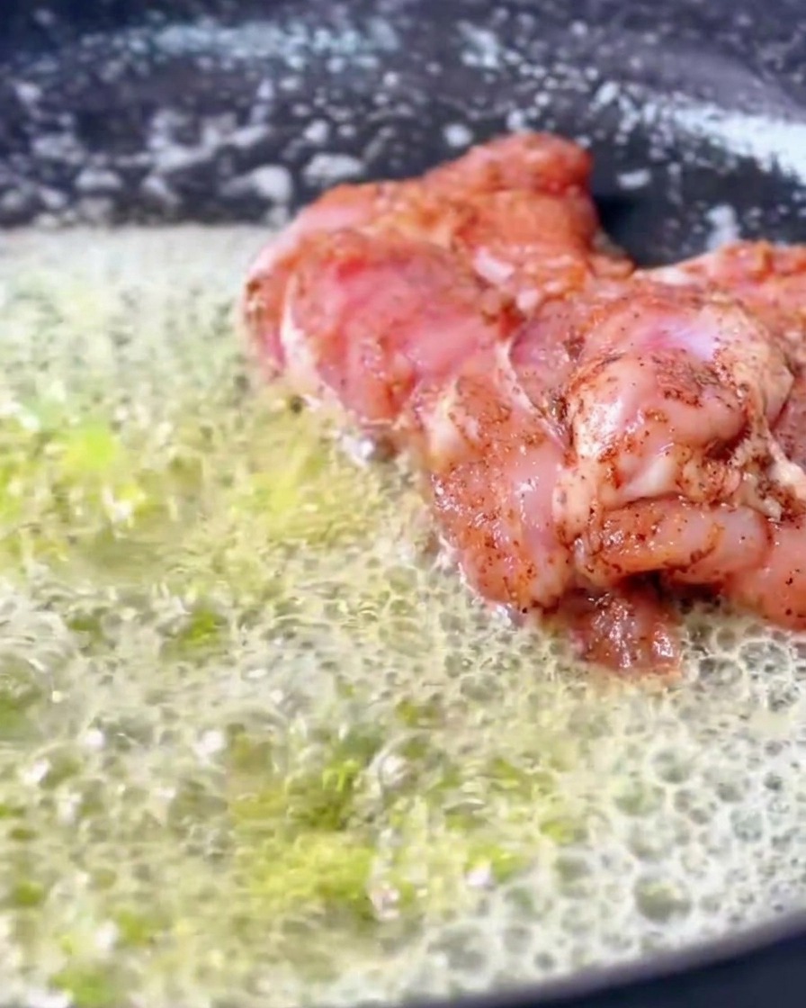 たっぷりの泡立つ溶かしバターが広がるフライパンの中で、下味をつけたケイジャンチキンがジュージューと焼けている様子。