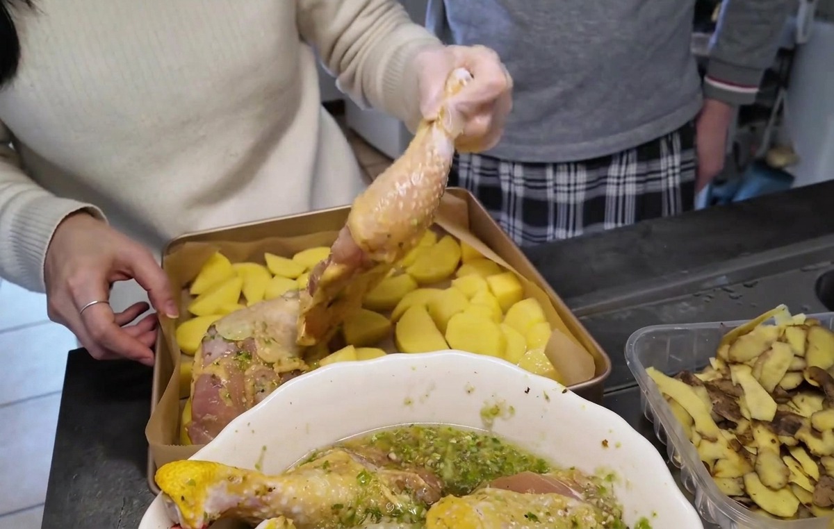 ゴールドの天板に敷き詰められたカットじゃがいもの上に、マリネされた生の鶏もも肉を皮目を上にして並べている様子。