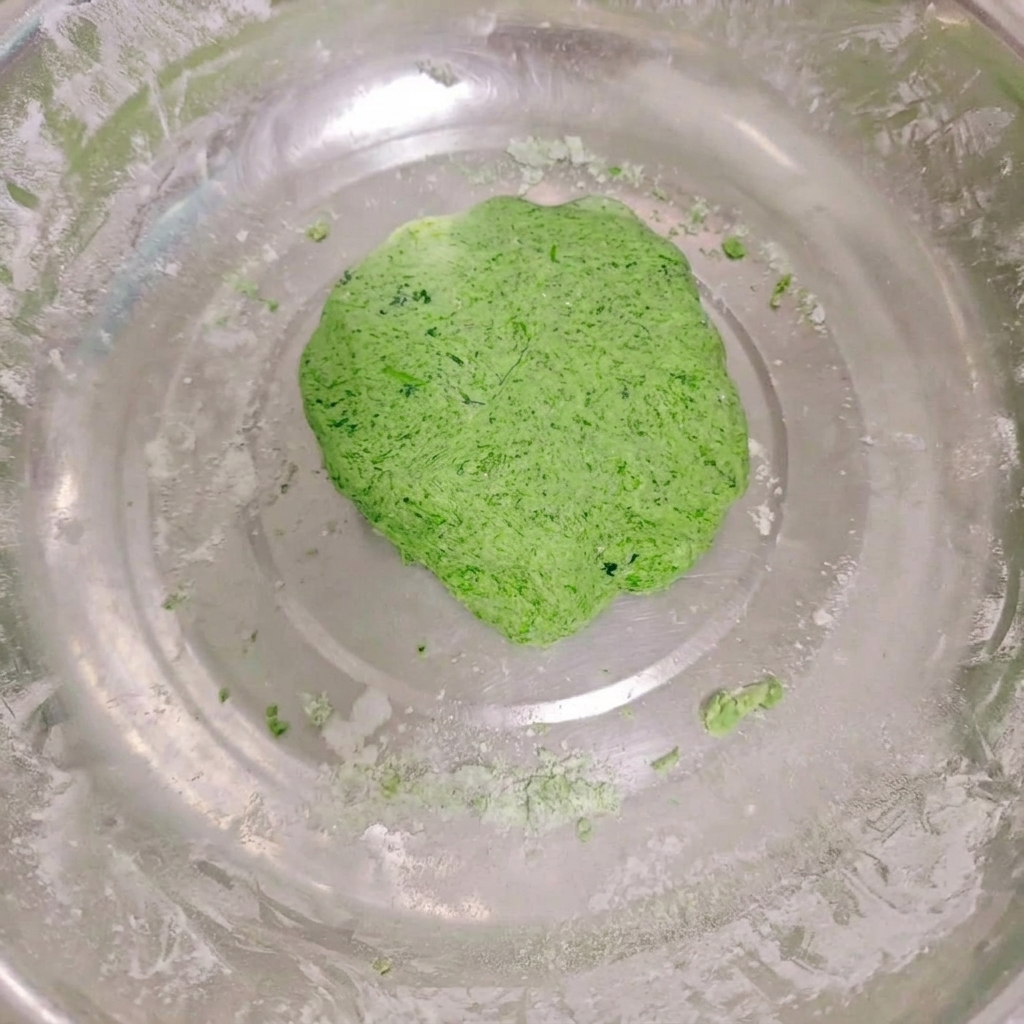 ステンレス製の大きなボウルの中で、なめらかにまとまった鮮やかな緑色の野菜生地の塊。