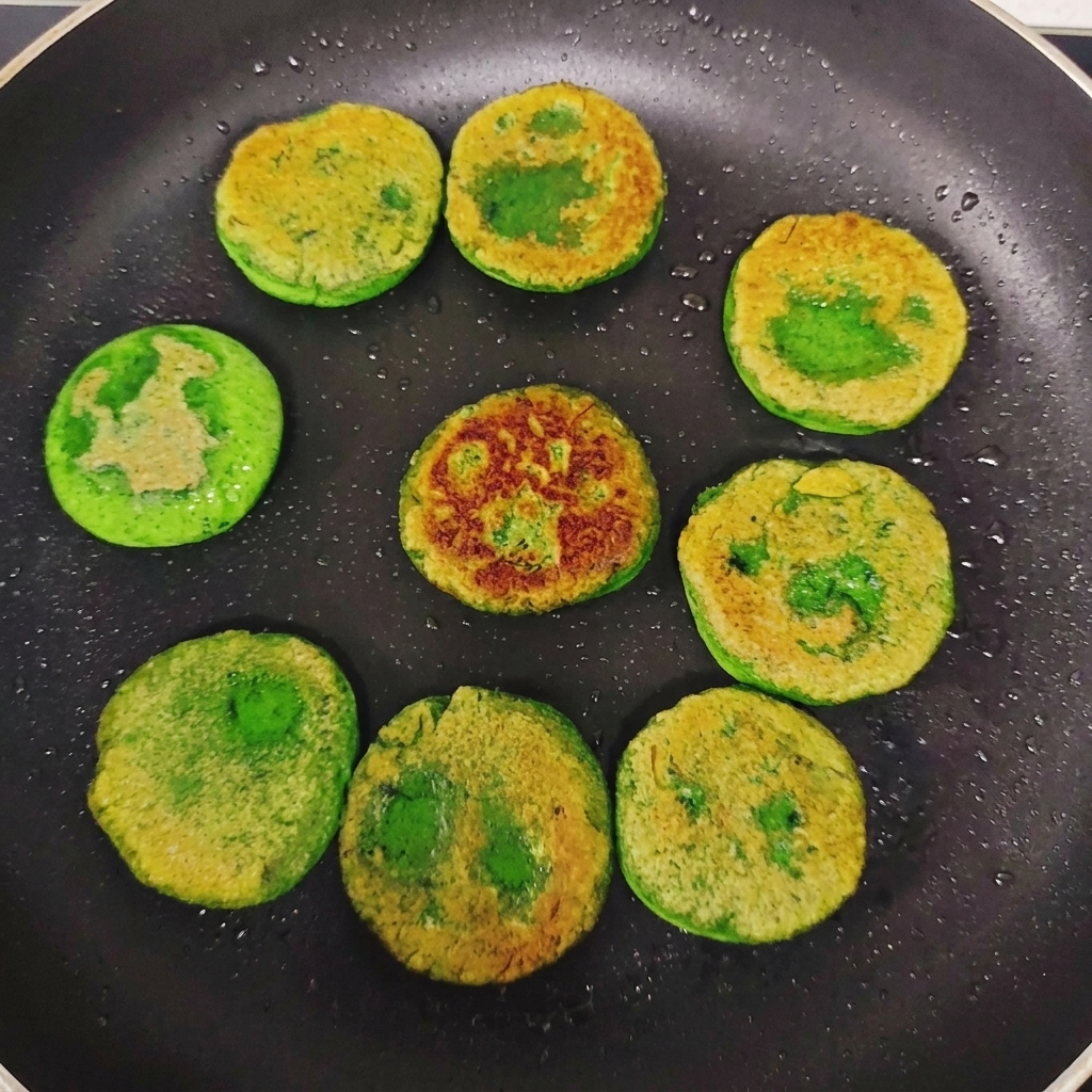 フライパンの中で裏返され、表面に美味しそうなきつね色の焼き目がまばらについた緑色の野菜おやき。