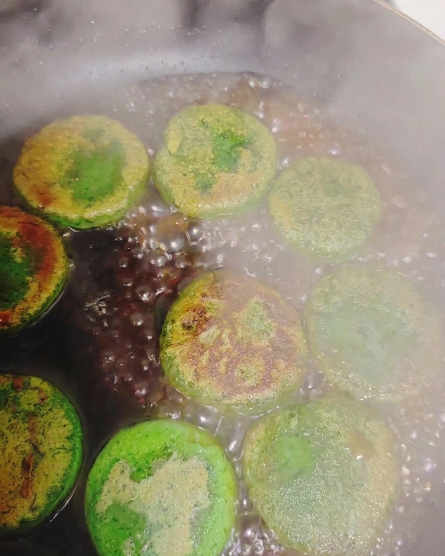 熱いフライパンの中で焼き色のついた野菜おやきの周りで、水が激しく泡立ち蒸気が上がっている様子。