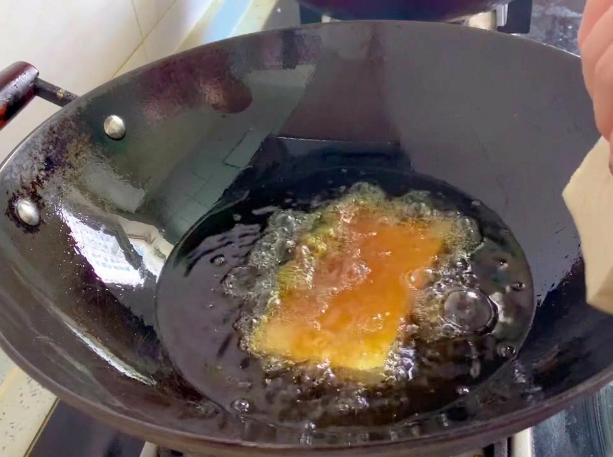グツグツと沸立つ油の入った中華鍋で、大きく切った豆腐を揚げている様子。