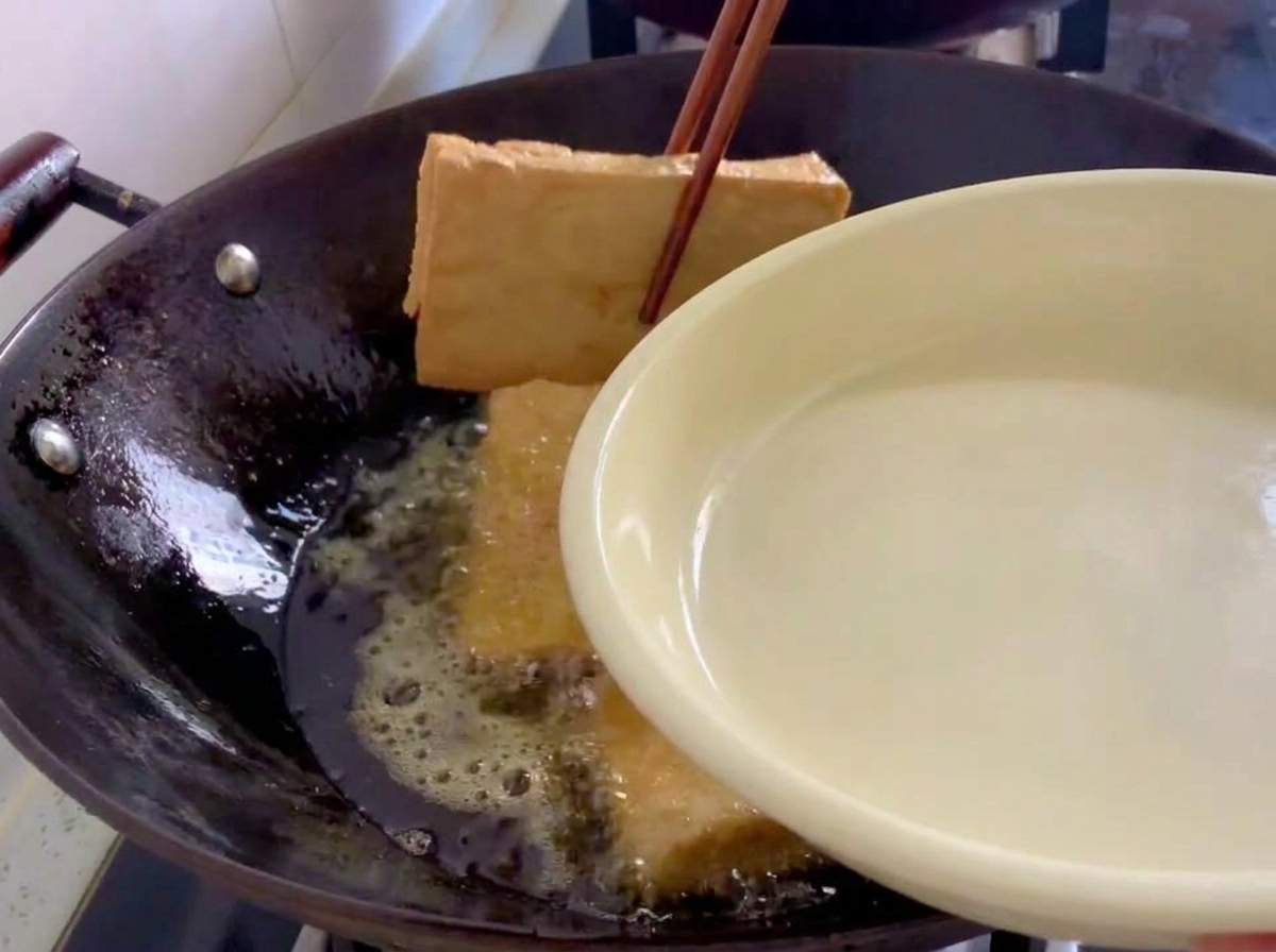 きつね色に揚がった豆腐を、菜箸で中華鍋から引き上げているところ。