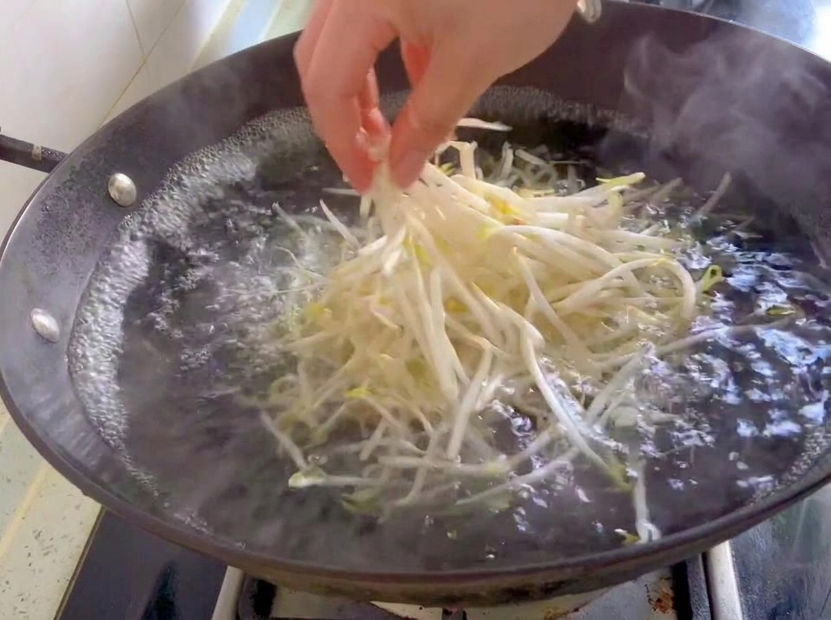 新鮮な白いもやしを、沸騰したお湯の入った中華鍋に入れている様子。