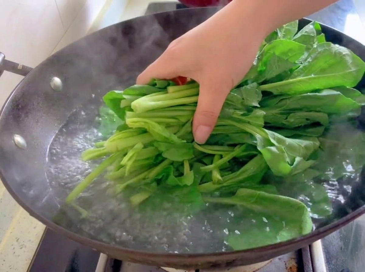 新鮮なほうれん草の束を、中華鍋の沸騰したお湯に入れているところ。