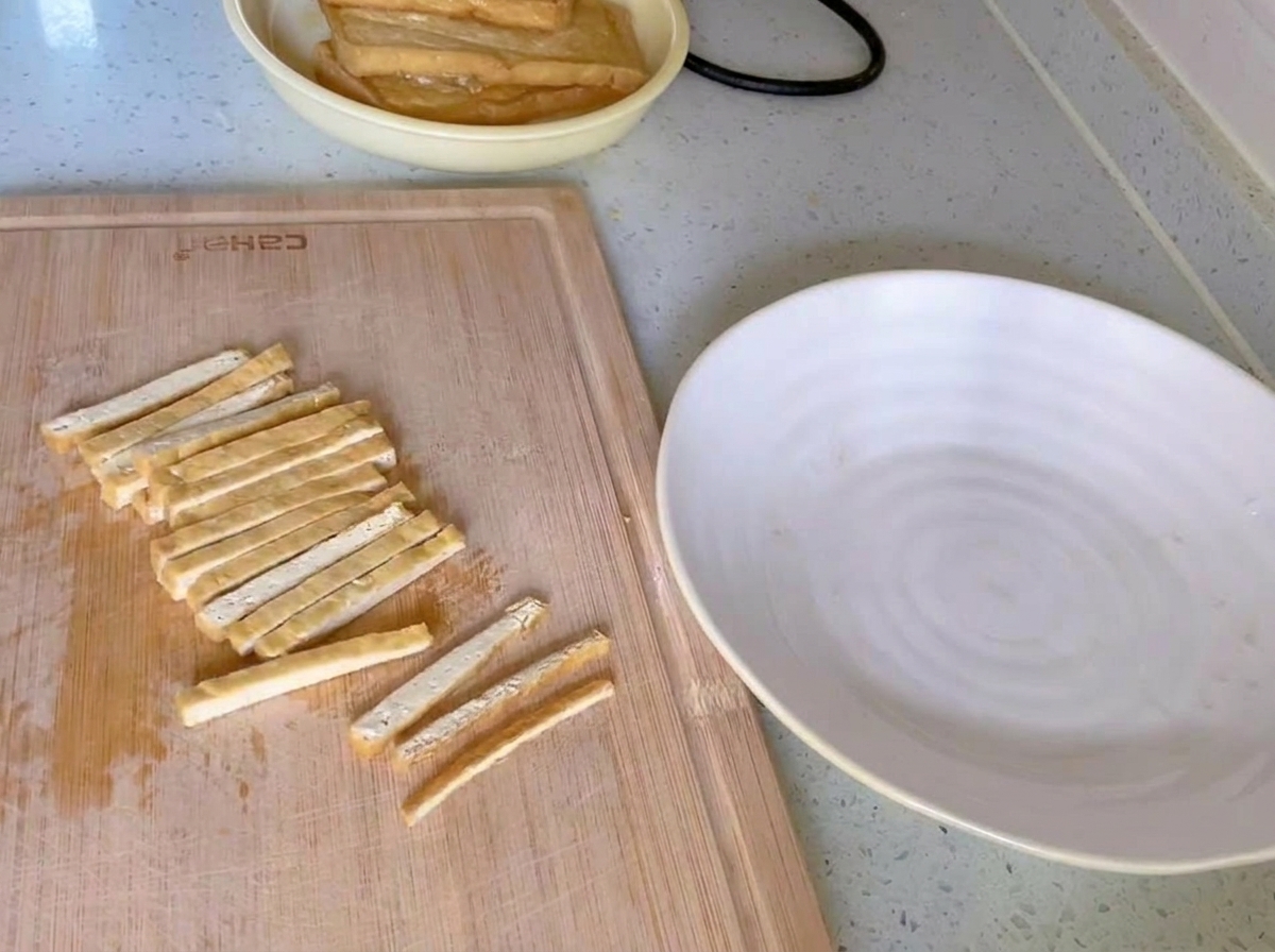 白いお皿の横に置かれた木のまな板の上で、きつね色の揚げ豆腐が均等な細切りにされている様子。