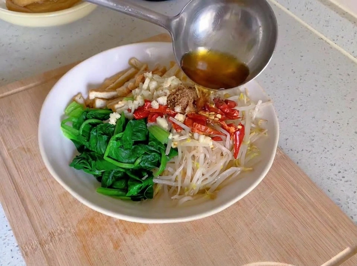 白熱した油をお玉で、野菜の上に盛られたみじん切りのにんにくと真っ赤な乾燥唐辛子にジュワッとかけているところ。