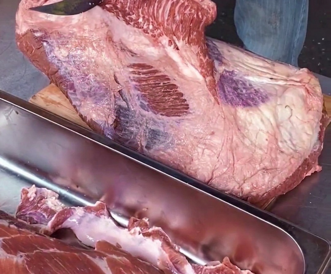 まな板に対して平行に鋭い包丁を入れ、白い脂肪の境目に沿って生のポイント肉とフラット肉を慎重に切り離しているシェフの手元のアップ。