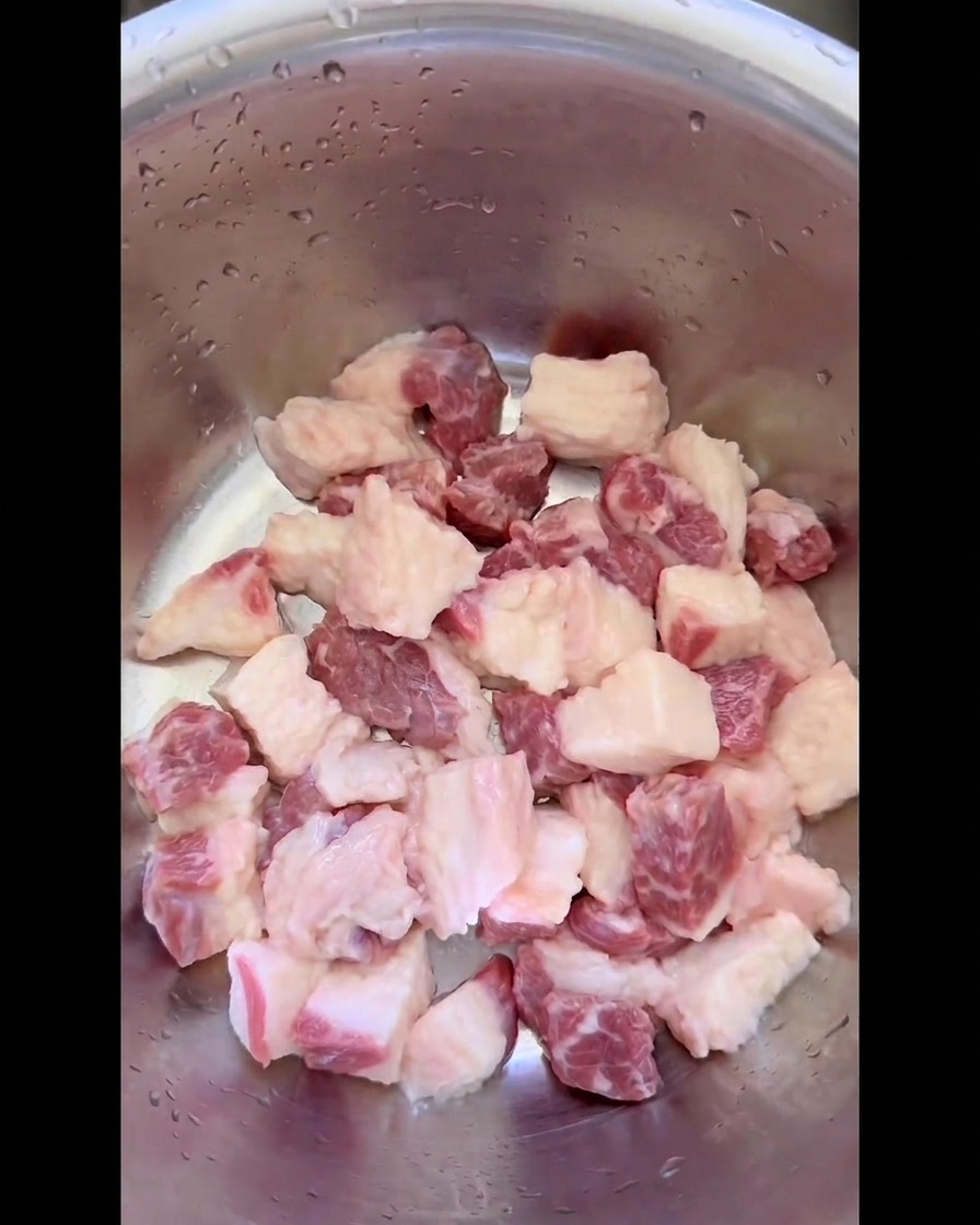 ステンレス製のミキシングボウルに入れられた、均一な小さな角切りにされた生の牛バラ肉の脂身。