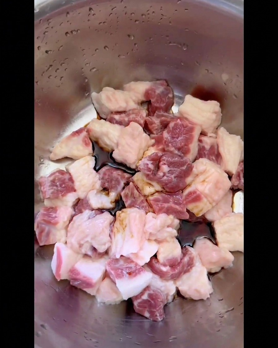 ステンレスボウルの中で、角切りにした生の牛バラ脂身の周りに注がれた中国たまり醤油などの液体調味料。