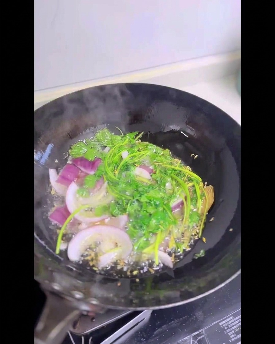 熱く熱した油が入った中華鍋の中で、パチパチと音を立てて揚がっている新鮮な緑のパクチーの茎とスライスした赤玉ねぎ。