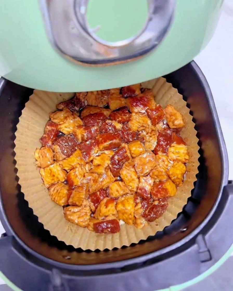 緑色のノンフライヤーのバスケット内に敷いた茶色いクッキングシートの上に、均一に重ならないよう一段に並べられた味付け済みの牛バラ脂身。
