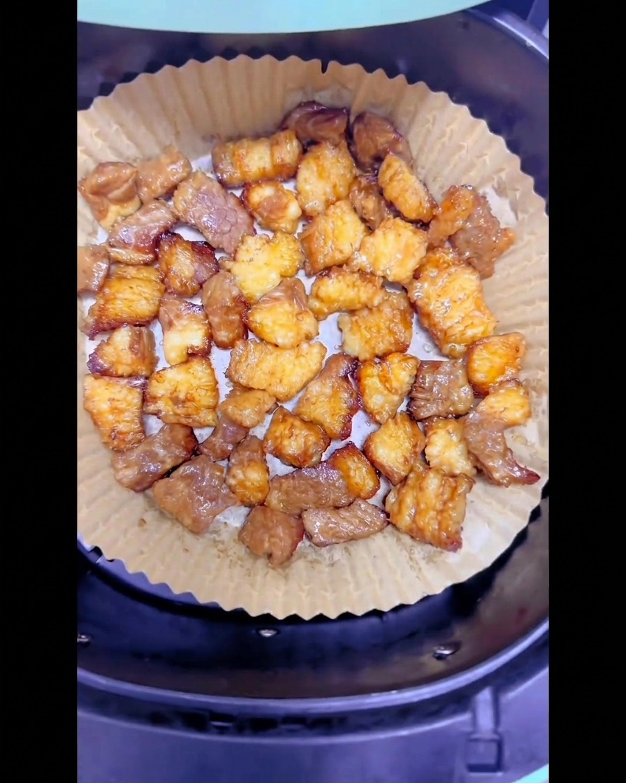 ノンフライヤーのバスケットに敷いた丸いクッキングシートの上で、適度に焼き色がついた牛バラ脂身が均一に並んでいる様子。