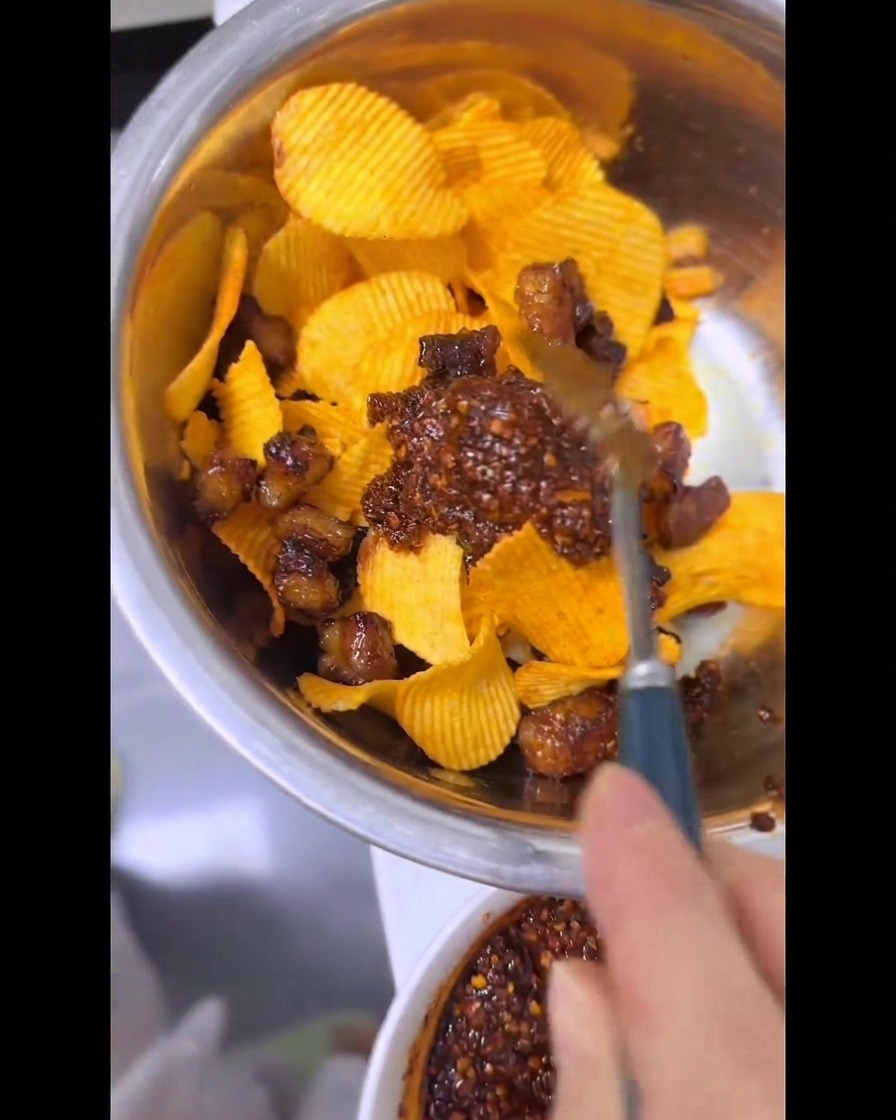 金属製のボウルの中で、ギザギザのポテトチップス、カリカリの牛脂、割と鮮やかな赤色の特製ラー油をスプーンを使って手際よく混ぜ合わせている様子。