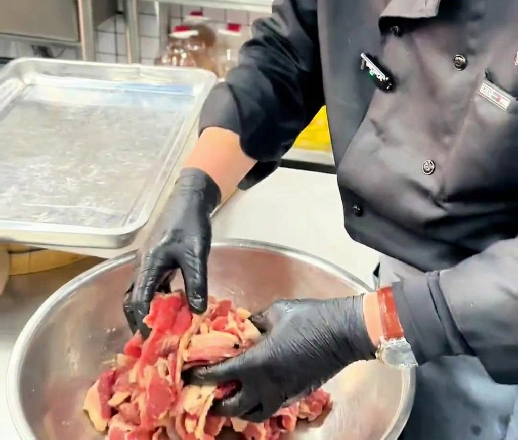 金属製のボウルの中で、薄切りの牛肉にしっかりと油を絡めながら全体を優しく混ぜ合わせている手元の様子。