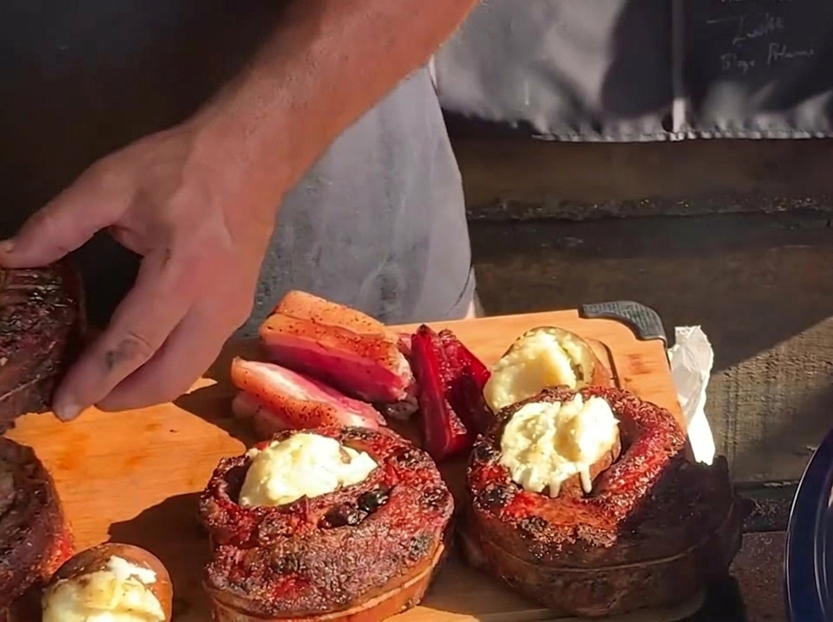 木のまな板の上で、焼き上がった丸いリブカップの空洞の真ん中に、熱々でバターの効いたローストポテトを詰めている手。