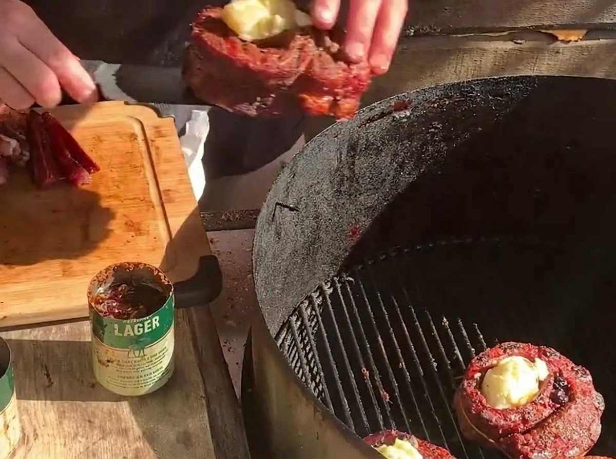ポテトを詰めたリブカップを炭火グリルに置き、その横にもう一つの肉のカップと厚切りベーコンを並べている様子。